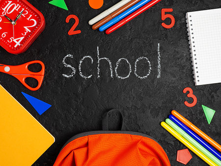 Orange backpack with school supplies on a black concrete background. The concept of the school. Copy...