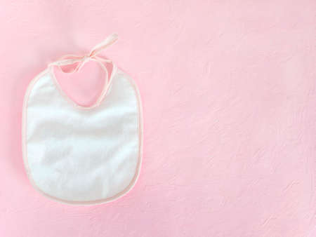 White baby bib with pink border, on pink background. The concept of feeding babies, children's theme.の写真素材