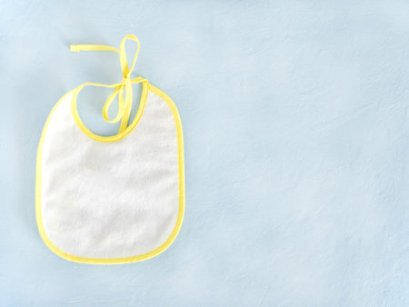 White baby bib with yellow border, on blue background. The concept of feeding babies, children's...