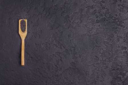 Black sesame on a wooden spoon on a black concrete background. Copy space.の写真素材