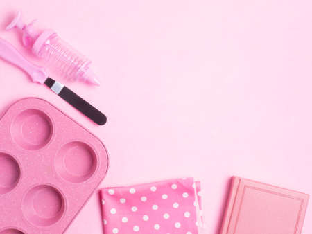 Cupcakes baking dish, a spatula, a recipe book, a towel on a pink concrete background. Monochrome. Copy space. Flat lay.の写真素材