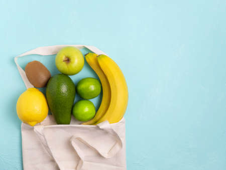 Various vegetables and fruits in an eco-friendly fabric bag on a blue background, top view. Concept of healthy nutrition, food background.A vegetable border with space for text. Vegan, vegetarian.の写真素材