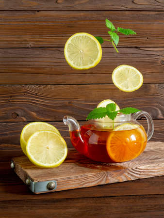 Glass teapot with tea, flying lemon, fresh mint leavesの写真素材