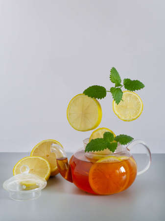 A glass teapot with tea, a flying lemon, fresh mint leaves on a gray background. Minimal concept of fresh natural teaの写真素材