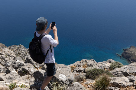 man taking pictures standing on a steep rocky shore by the sea, Greece, Creteの写真素材