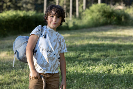 A boy with a bag stands on the edge of the forestの写真素材