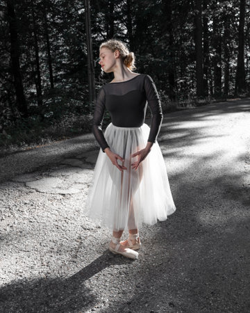 A young ballerina stands in a ballet position on the roadの写真素材