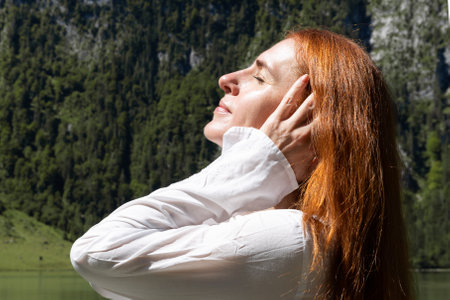 A beautiful red-haired woman with her eyes closed enjoys a warm summer day and good weather.の写真素材
