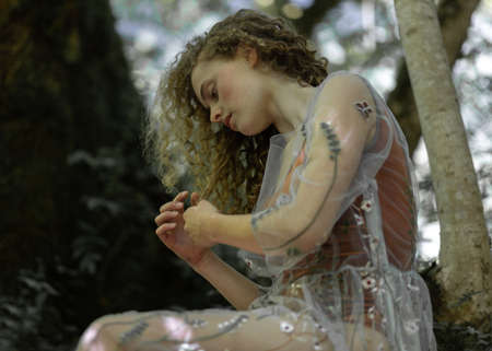 Beautiful girl with long curly hair sits on a treeの写真素材