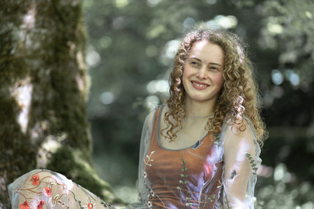 Portrait of a young long-haired curly pretty model with a smile on her face on a background of greeneryの写真素材