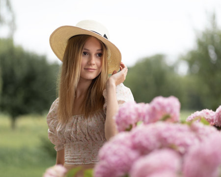 Young model posing in a straw hat next to a large hydrangea bush against the backdrop of treesの写真素材
