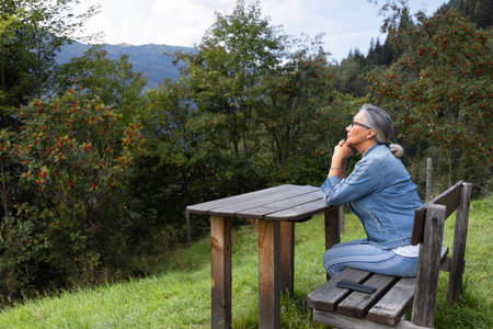 A gray-haired woman sits at a wooden table, in an alpine setting.の写真素材