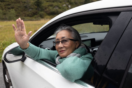 A gray-haired lady looks out of a car window and waves her handの写真素材