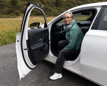 A gray-haired lady gets out of a car and smiles at the cameraの写真素材