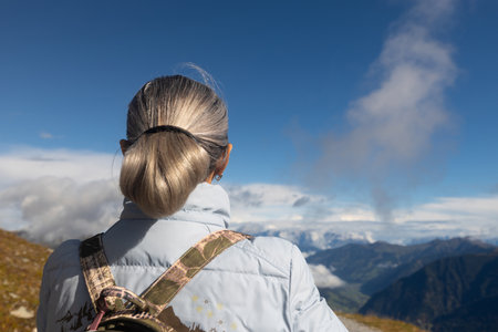 A gray-haired woman stands at the level of clouds in the alpine alps, rear viewの写真素材