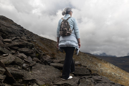 A woman climbs up a rocky mountain path against the background of clouds, the Austrian Alps