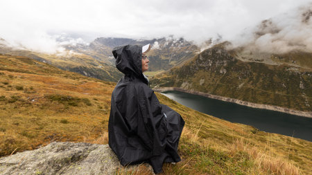 A woman sits on a stone high above a mountain lake against the backdrop of clouds. Austria, Alpsの写真素材