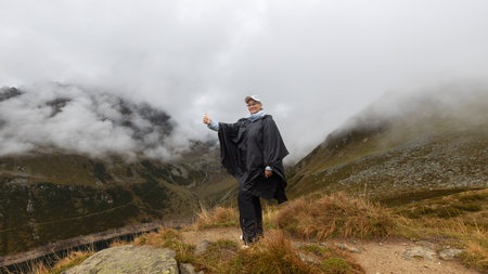 A woman stands at a height above a mountain lake on a path against the background of clouds. Austria, Alpsの写真素材