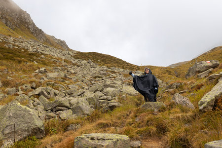 A satisfied woman in a rain cape descends from the pass along a mountain path. Austria, Alpsの写真素材