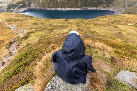 A woman is resting on a rock high above a mountain lake. Austria, Alps