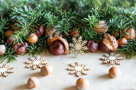 Green branches with nuts scattered on fir branches and snowflakes made of wood lie on craft paperの写真素材
