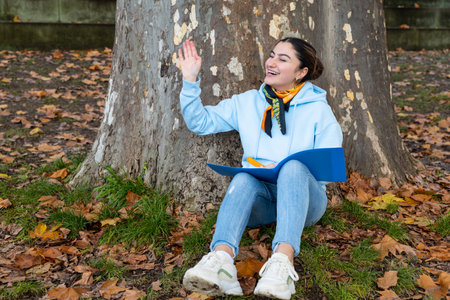 An oriental girl sits under a tree with a blue folder in her hands and laughs, Austriaの写真素材