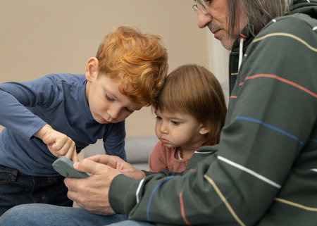 A grandfather with grandchildren, a red-haired boy and a blonde girl, looking at the phone
