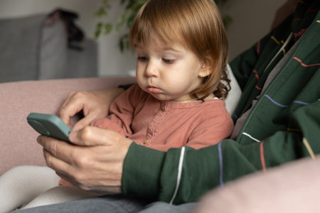 A little girl sits in her arms. an adult in a home chair and is surprised by what he sees on his...