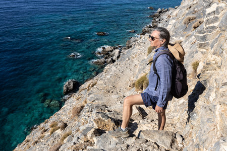 Grizzled long-haired man stands on a trail on a steep rocky shore, Greece, Creteの写真素材