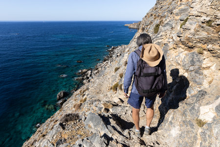 A grizzled man walks along a rock trail high on the sea, Greece, Creteの写真素材