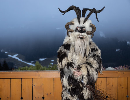 Krampus, the hero of Christmas legends, in a skin and a horned mask stands at a wooden fence,...