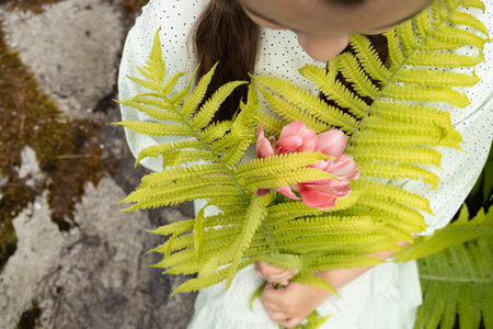 The girl sits on the stone steps and holds in her hands a bouquet of fern leaves and a tulipの写真素材