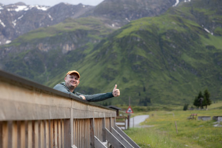 A young man stands on a wooden bridge in a great mood in the alpine valley of Sportgastein, Austriaの写真素材