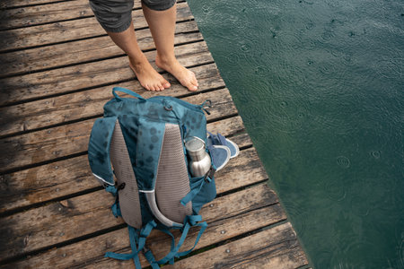 Womens bare feet and backpack on coastal bridge in the rain, the concept of ecotourism, economical outdoor recreationの写真素材