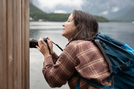 Young female photographer shooting on a lake behind a wooden wall, creative concept, Hallstatt, Austriaの写真素材