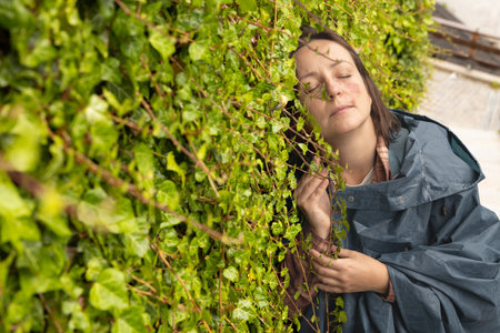 A young woman with a spot on her face stands against a green living wall, pressed against itの写真素材