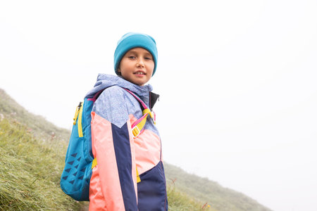Little smiling girl in bright clothes walking in the mountains on a foggy day