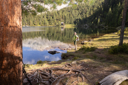 A man with a backpack stands on the shore of a beautiful lake with a reflection among a coniferous forest: Austriaの写真素材