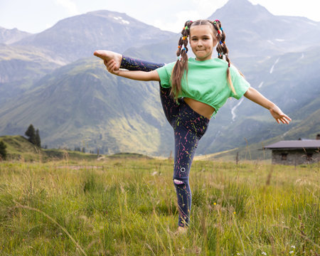 A girl with mischievous pigtails resting in the mountains, doing stretching in a mountain meadow in an Austrian valleyの写真素材