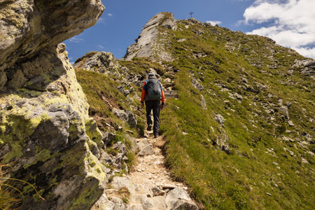 Man on a difficult stretch of rocky road to the top with a cross on the background of the sky, Austriaの写真素材