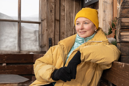 Close-up portrait of a middle-aged woman in winter clothes sitting on bench near house against the background snowdriftの写真素材