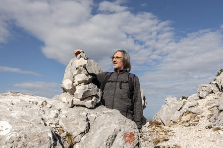 Gray-haired long-haired man with a smile on his face building a tower of stones of different sizes, Austriaの写真素材