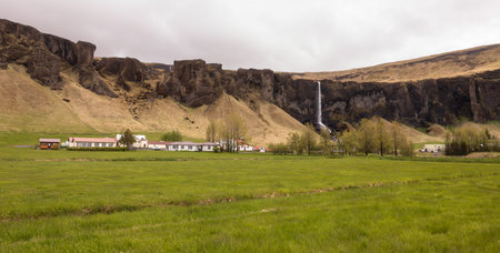 Rural Icelandic Farm With Waterfall and Dramatic Cliffsの写真素材