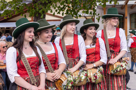 AUSTRIA, DORFGASTEIN - 1 MAI, 2024: Women In Traditional Dirndl Dresses Holding Flower-Adorned Kegs...