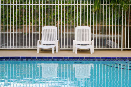 white plastic loungers along the fence on a pool deckの写真素材