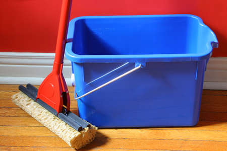 mop and blue bucket on hardwood floors with red wall in backgroundの写真素材