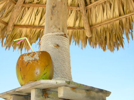 tropical coconut cocktail under beach umbrella on a sandy beach