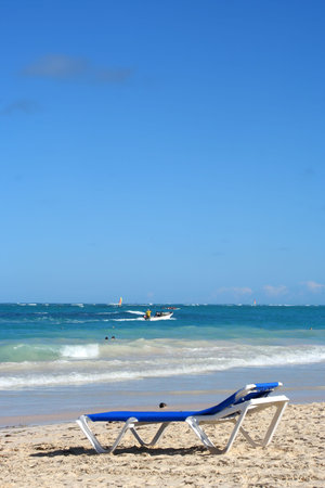 empty beach chair overlooking the ocean with boat on the Caribbean shore of Bavaro beach, Punta Cana...