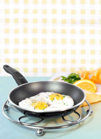 two sunny side up eggs in frying pan with cut up orange on cutting board in the backgroun ready for breakfastの写真素材