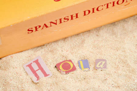 spanish hello 'hola' on sandy tropical beach with spanish dictionary in the backgroundの写真素材